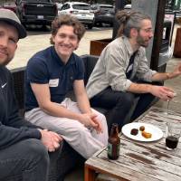 Three alumni chat a table outside